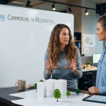 Two women discussing commercial to residential conversion with architectural models in modern office setting